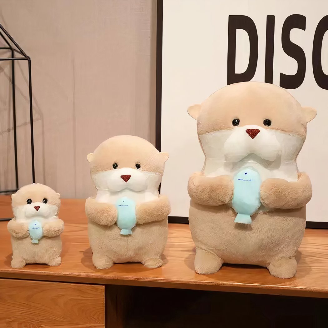 Three beige otter plush toys holding a light blue fish on a wooden table.